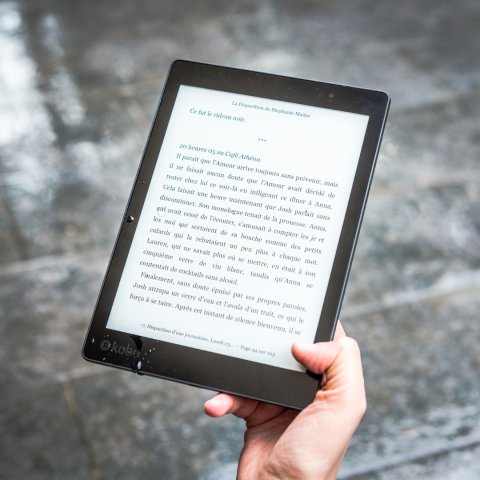 partial view of a hand holding an e-reader against a gray background